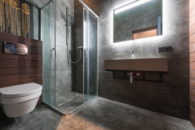 Modern bathroom with a glass shower stall, floating concrete sink, and wall-mounted toilet against grey tiled walls.